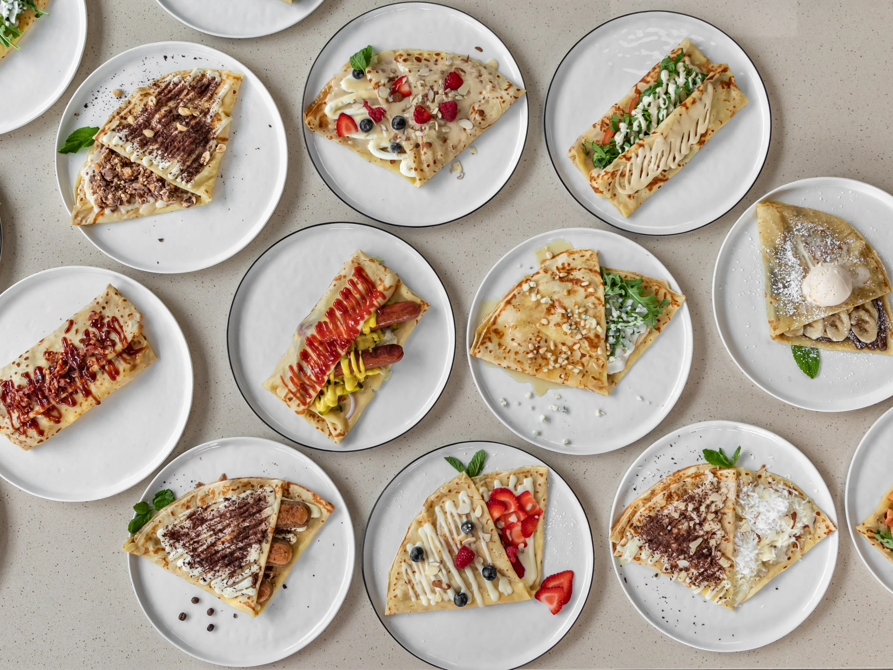 Variety of sweet and savory crepes on white plates