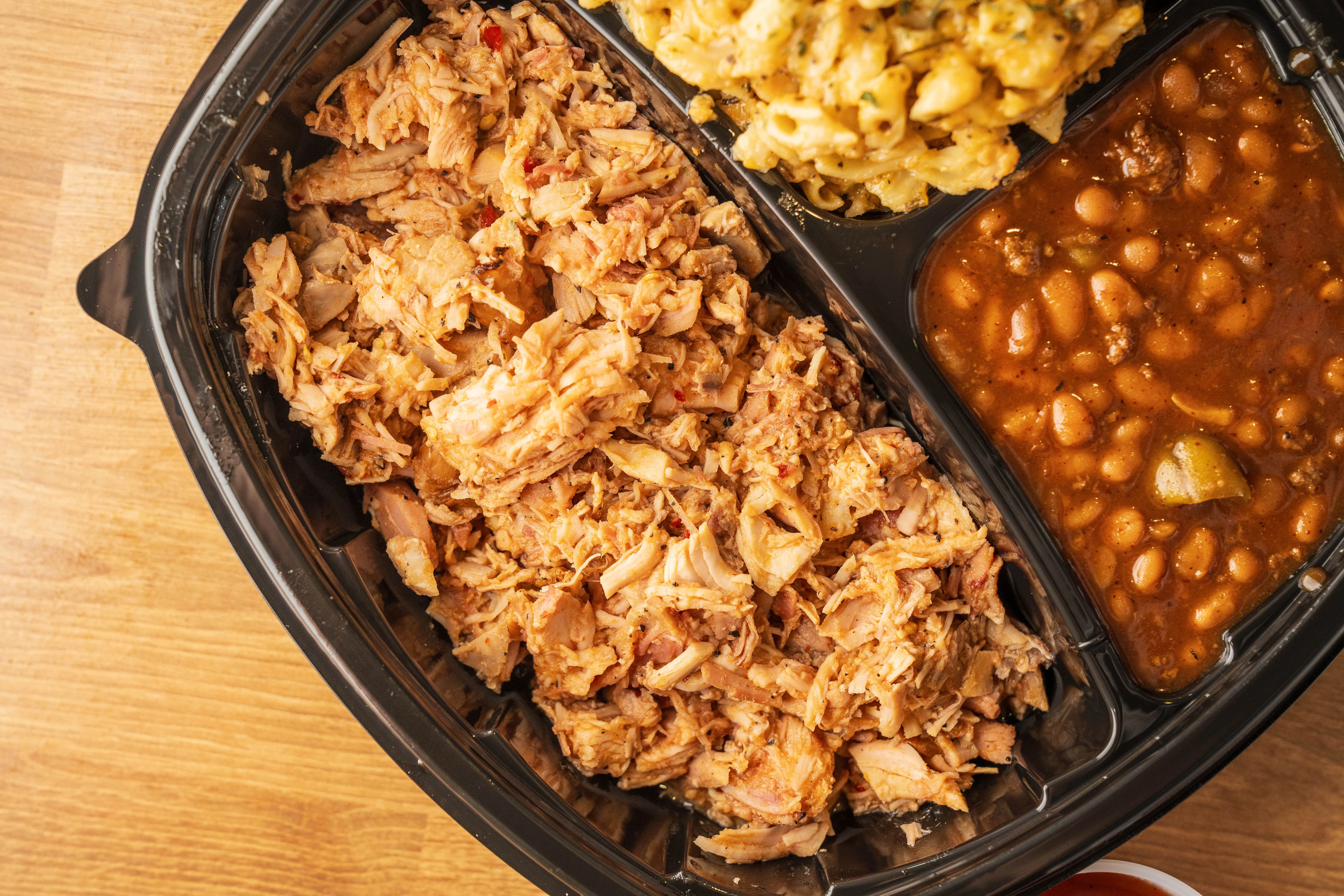 A meal container filled with shredded meat, macaroni and cheese, and baked beans. The items are neatly arranged in separate compartments.