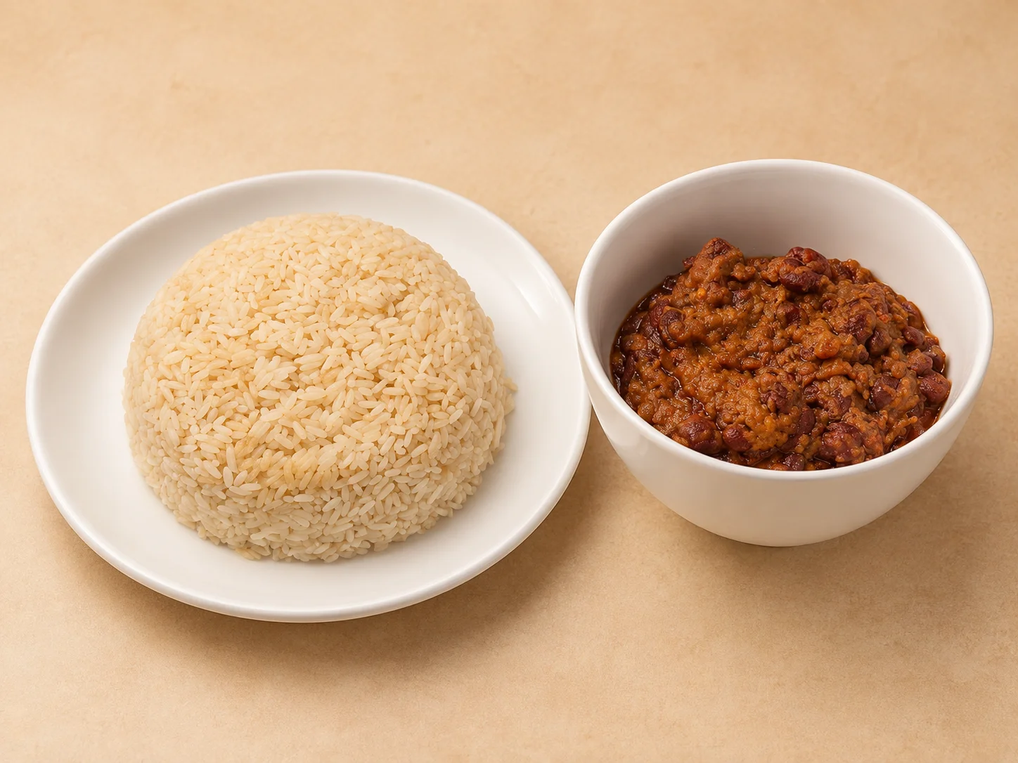 A serving of rice is presented on a plate alongside a bowl of chili-style bean dish. The rice is fluffy and well-cooked, while the beans are rich in color and texture.