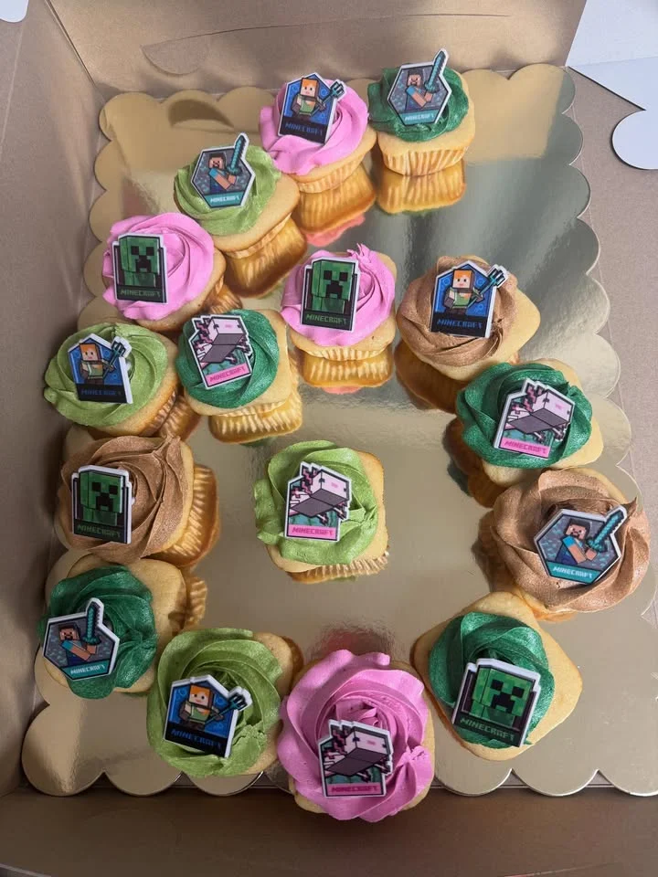 A beautifully decorated box of cupcakes, each topped with colorful frosting and themed decorations.