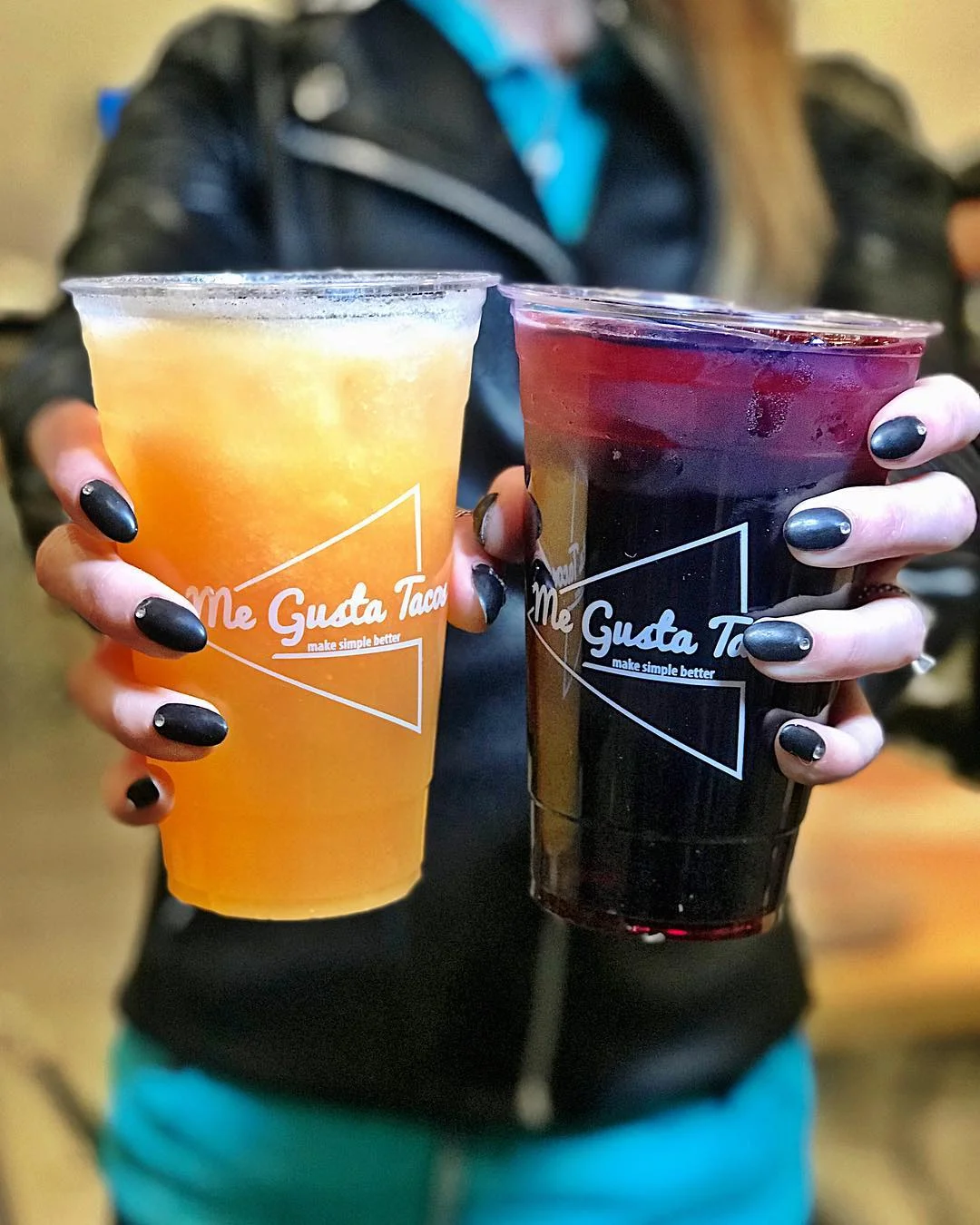 Two colorful beverages served in clear cups, one orange and one dark red, held together.
