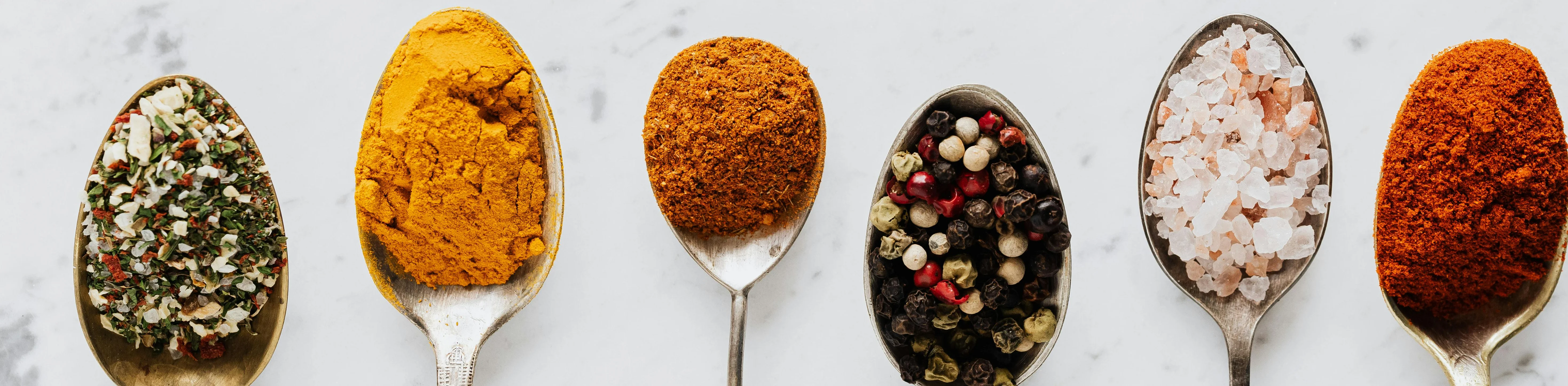 Variety of spices in vintage spoons on marble surface