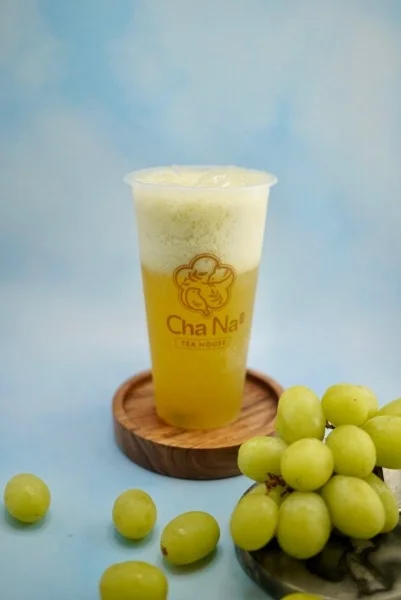 A refreshing golden beverage with a frothy top, accompanied by a bunch of green grapes on the side.