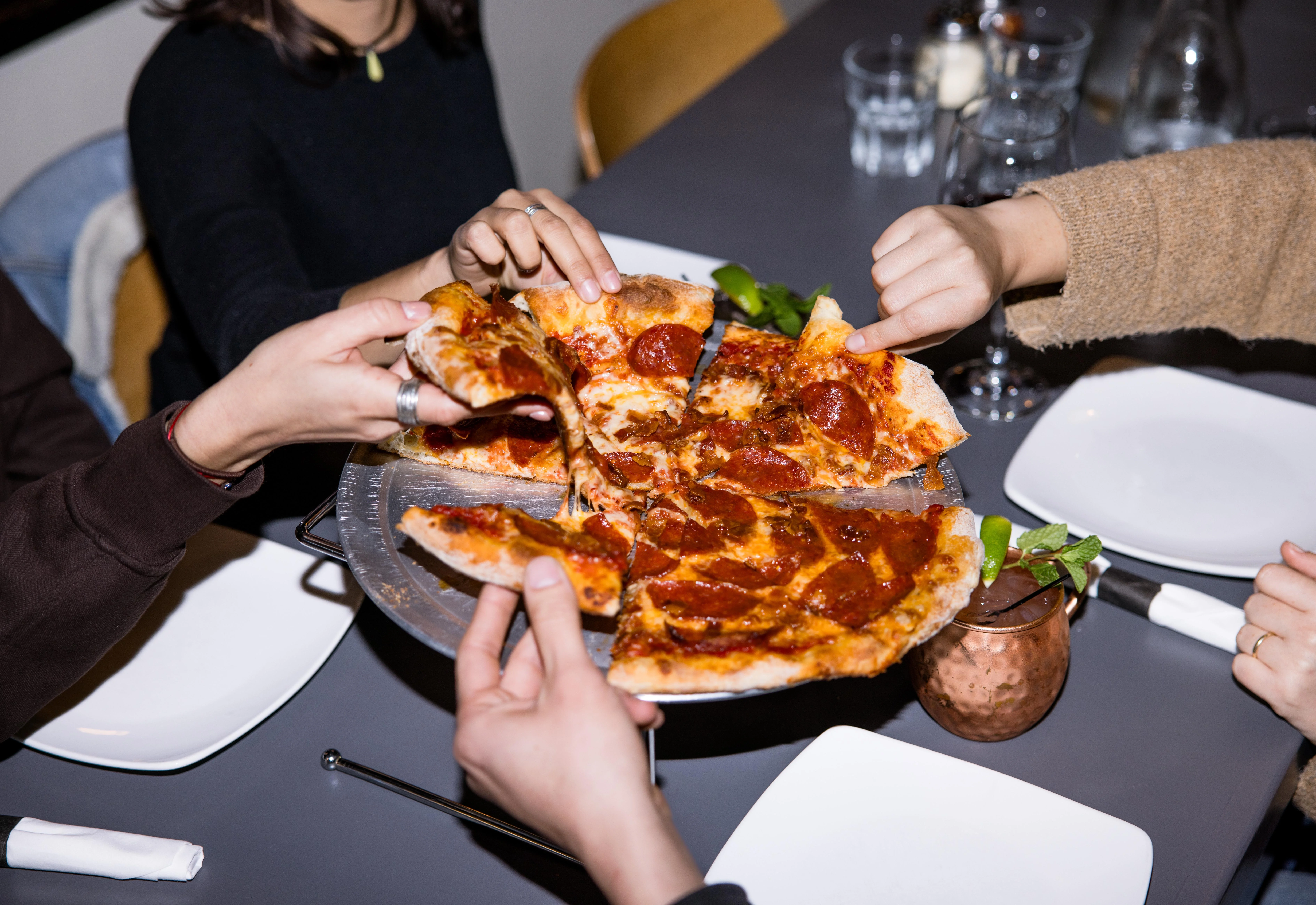 A group of people sharing a delicious pepperoni pizza adn some drinks