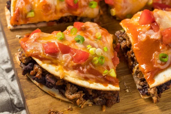 A delicious spread of loaded nachos, with melted cheese, seasoned beef, and fresh toppings like tomatoes and green onions served on a wooden board.