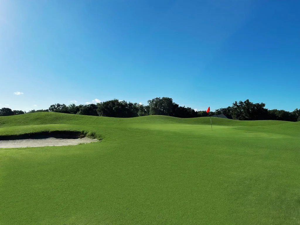 Lush green golf course with a sand trap and flag under a clear blue sky