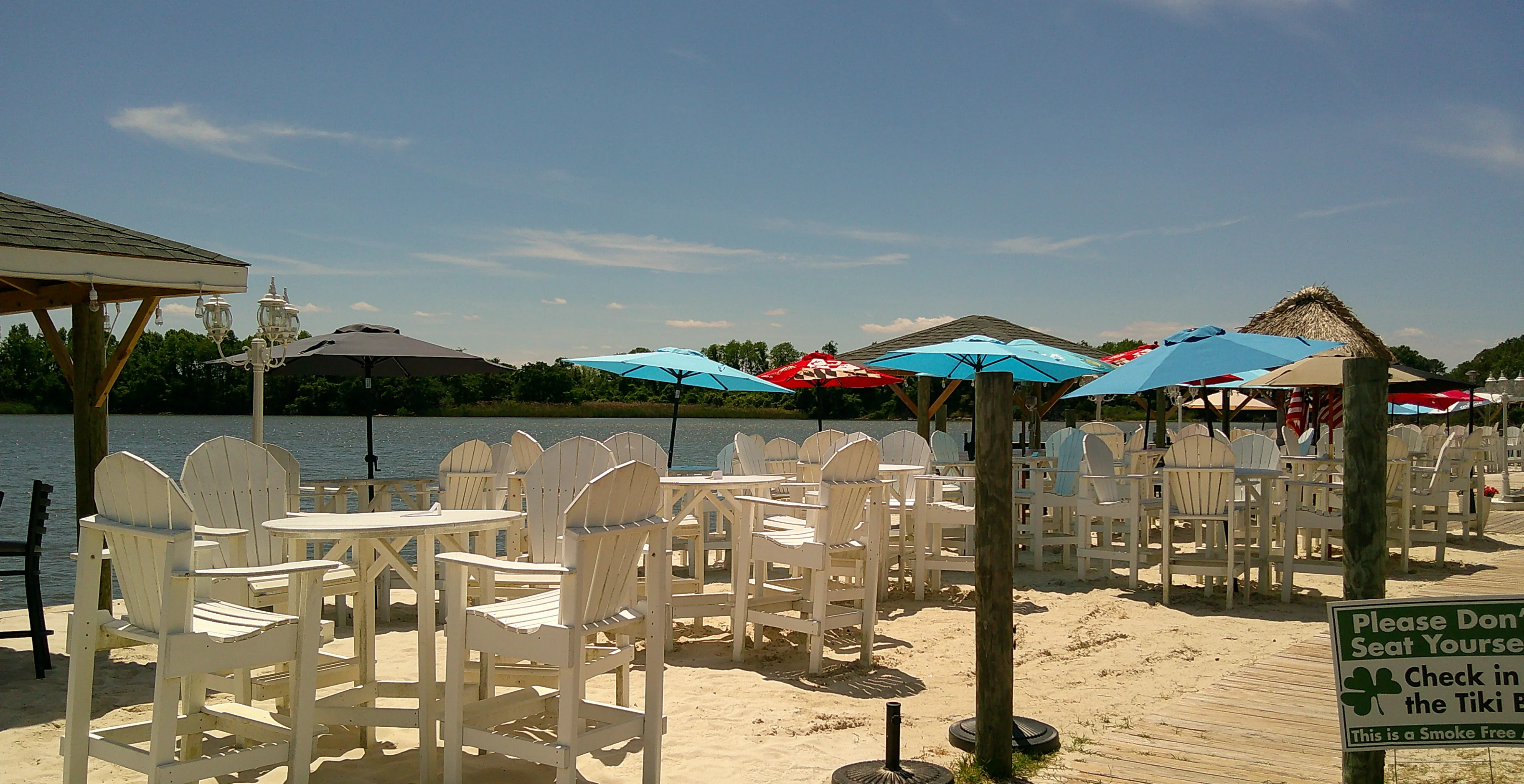 Outdoor dining area by the water with white chairs and colorful umbrellas.