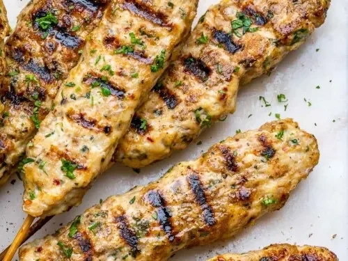 Grilled Turkish kebabs garnished with herbs on a white platter