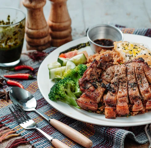 Grilled pork chop with vegetables and rice, served in a rustic setting