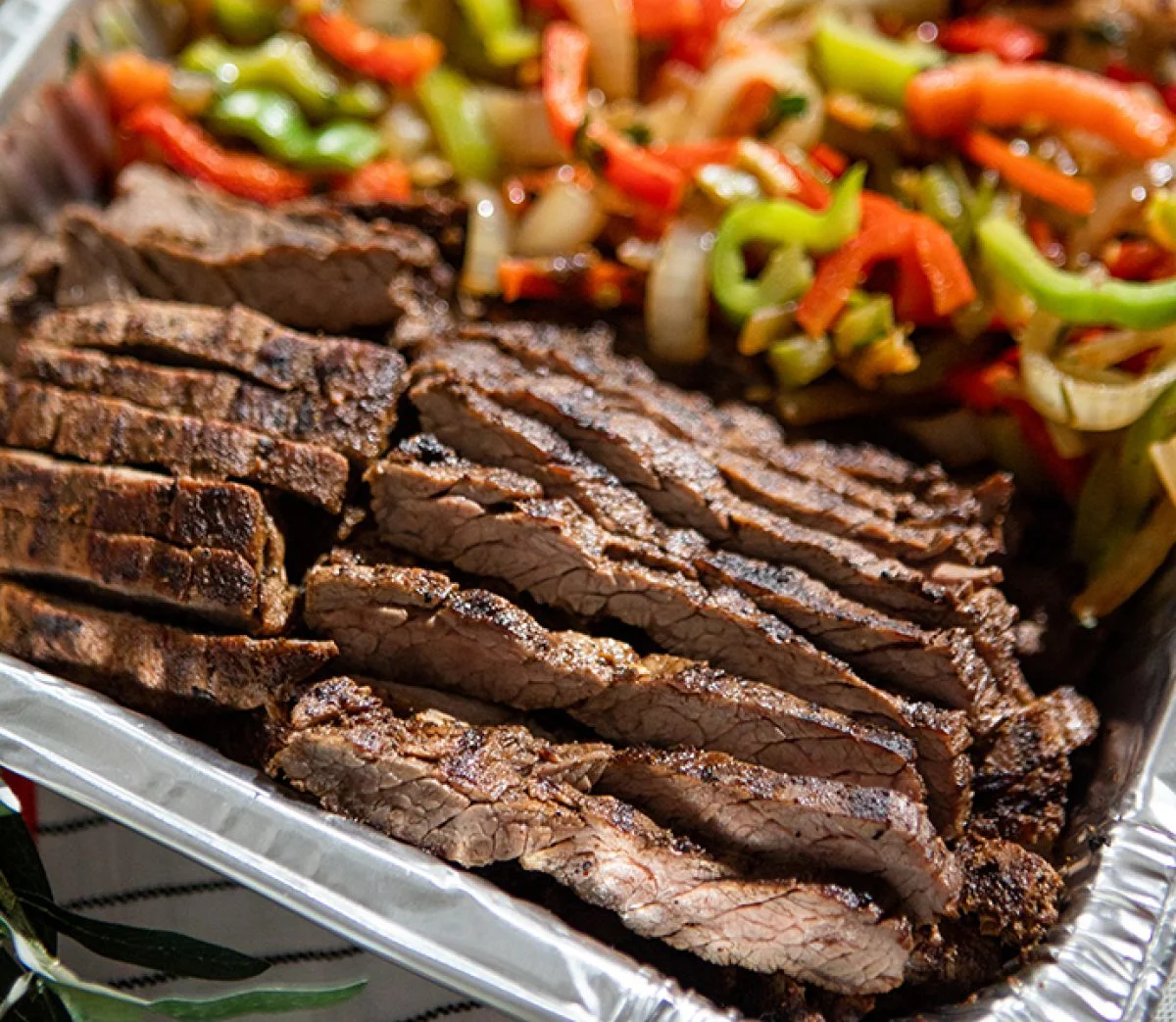 Sliced beef brisket arranged neatly in a tray, accompanied by a colorful mix of sautéed peppers and onions.