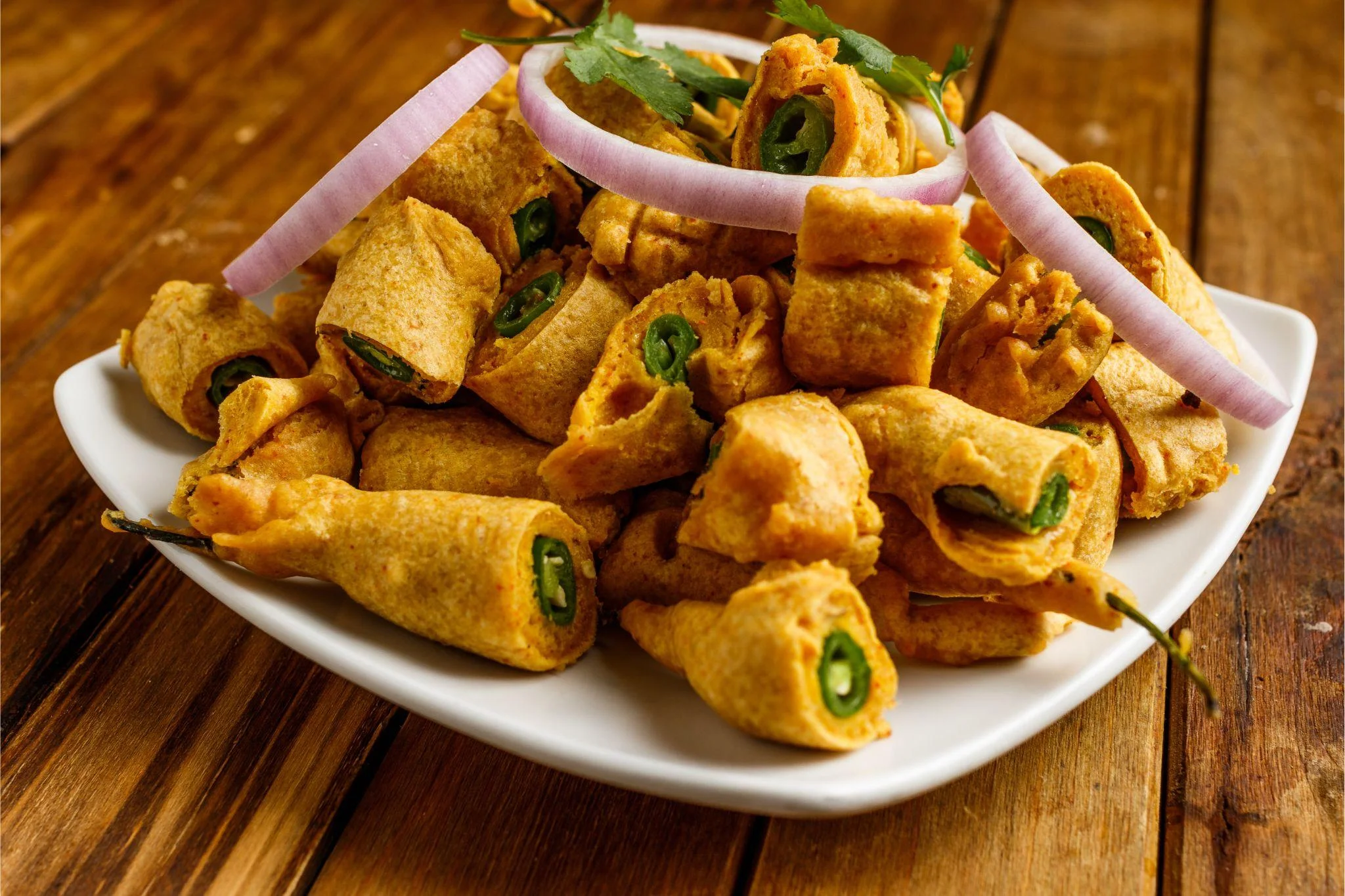 A plate of crispy fried snacks shaped like rolls, garnished with onion and herbs.