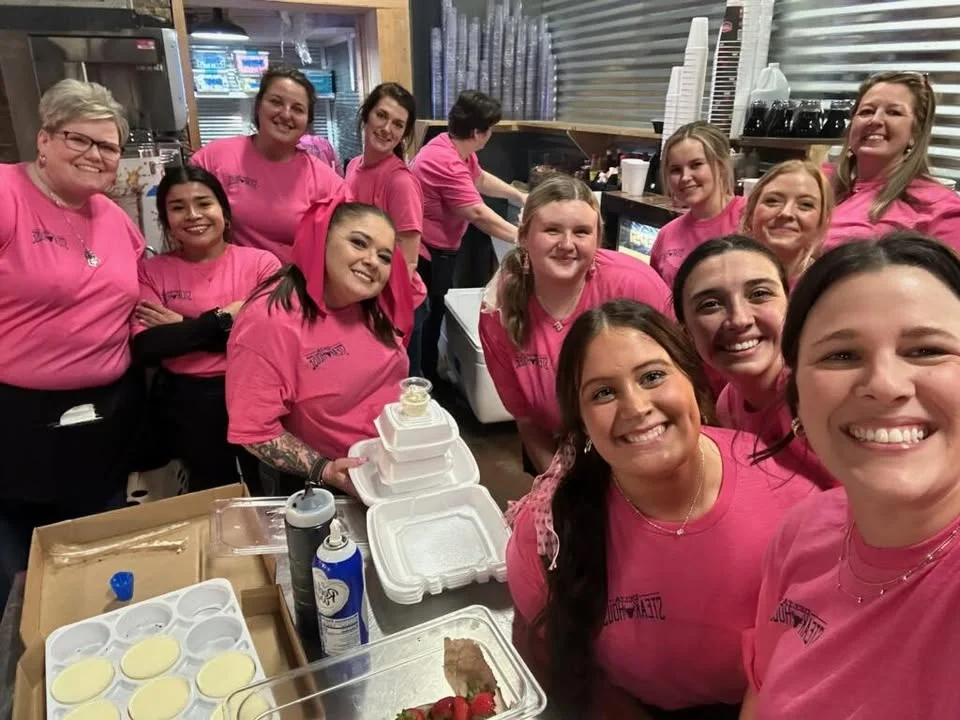 Group of restaurant staff in pink shirts smiling together in the kitchen