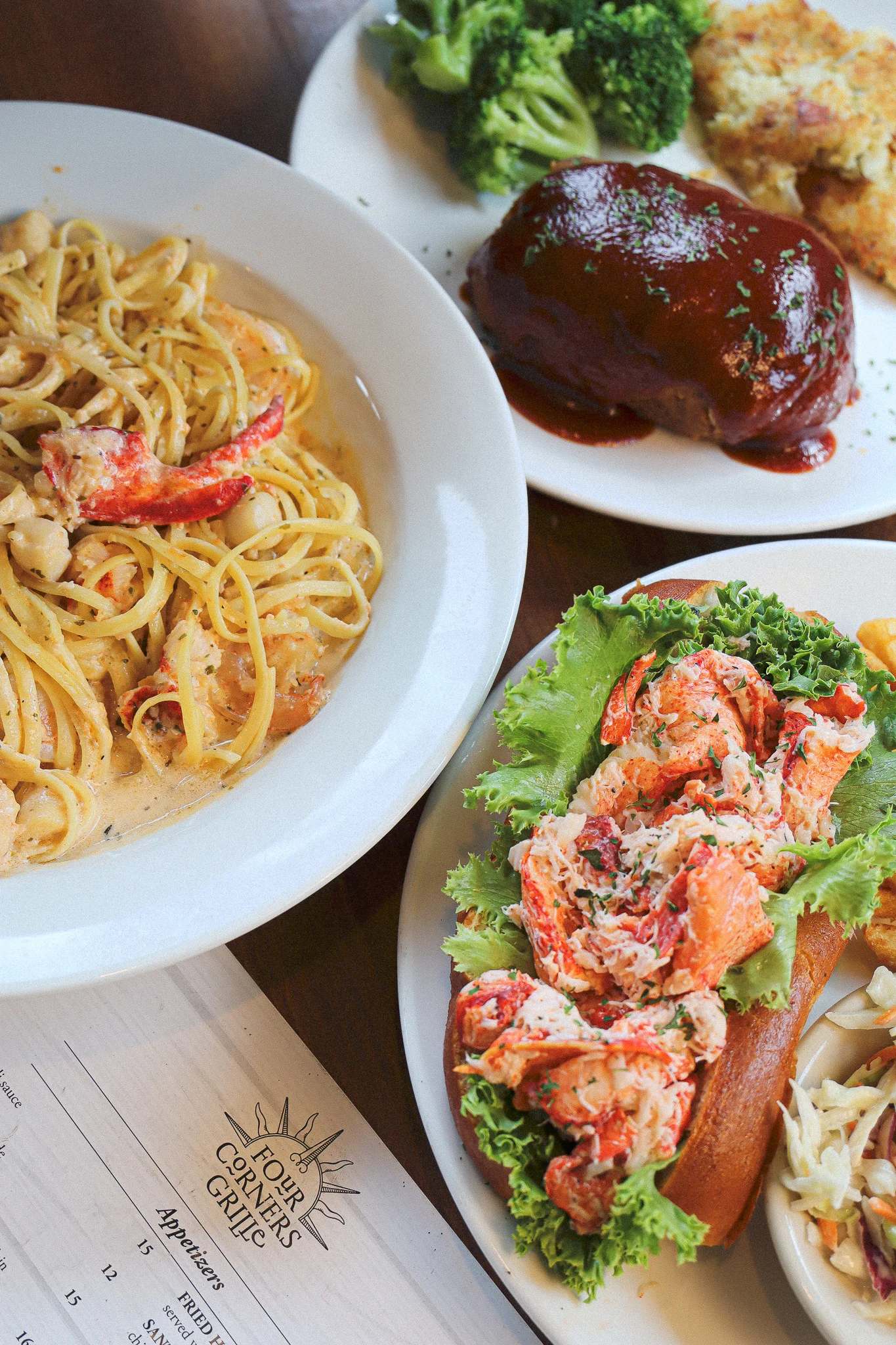 Image of three dishes from Four Corners Grille of a lobster roll, seafood saute, and meatloaf, on top of the menu