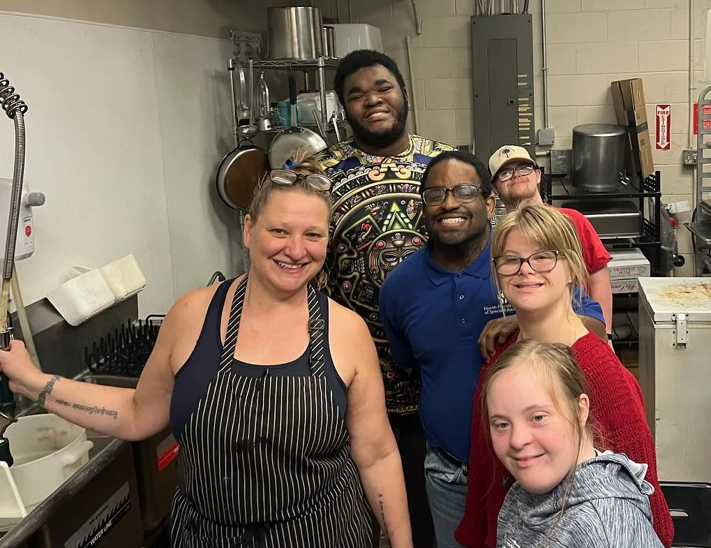 Team of chefs smiling in a busy restaurant kitchen