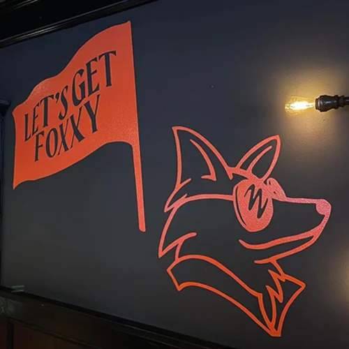 Playful 'Let's Get Foxxy' neon flag with fox logo in The Fox's Den, Carson City—highlighting the foxy, hidden hotspot atmosphere at The Fox Restaurant & Brewery