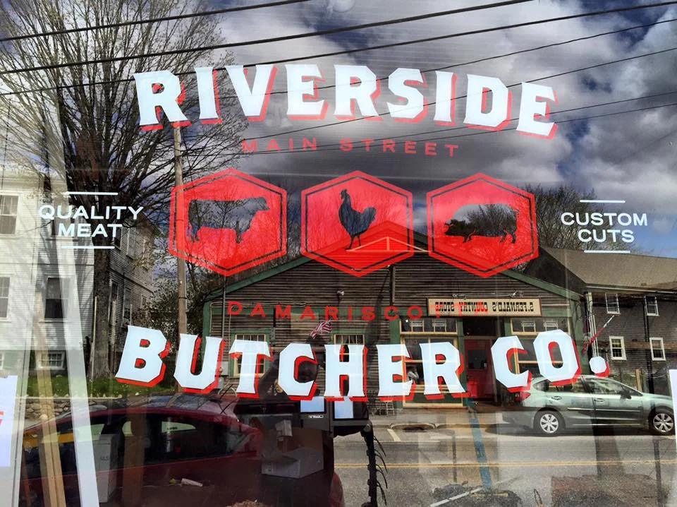 A storefront sign displaying the name of a butcher shop along with icons representing different types of meat.