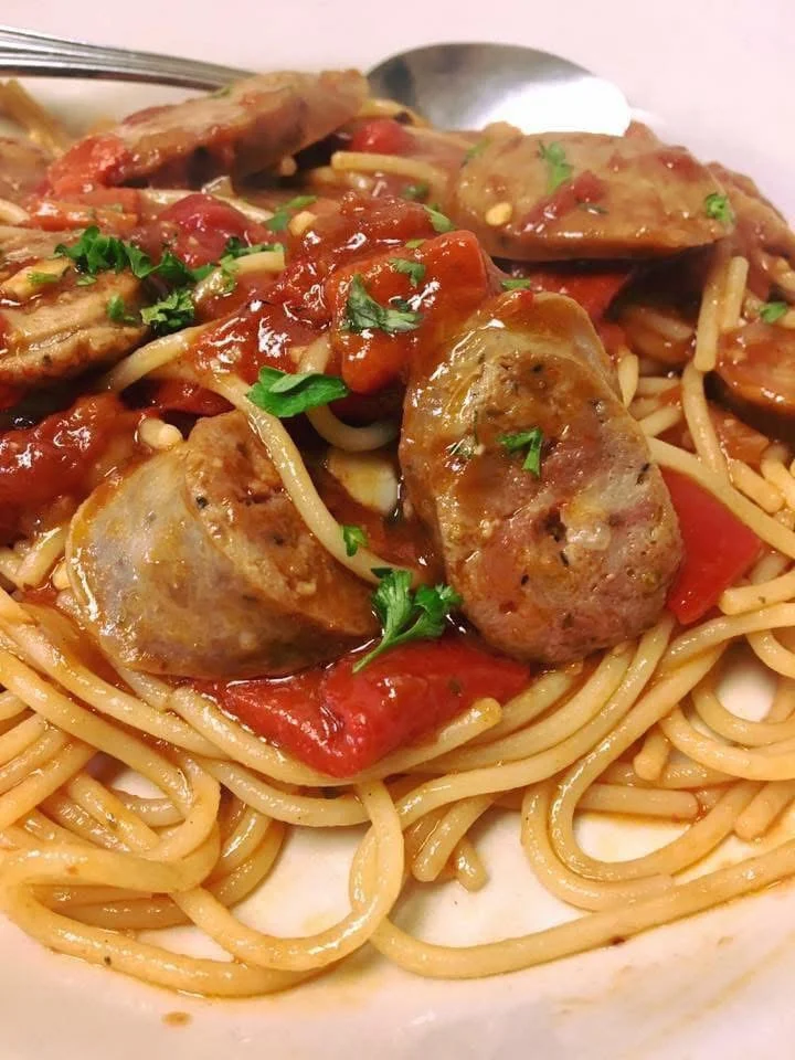 A plate of spaghetti topped with sausage slices and a rich tomato sauce, garnished with fresh parsley.