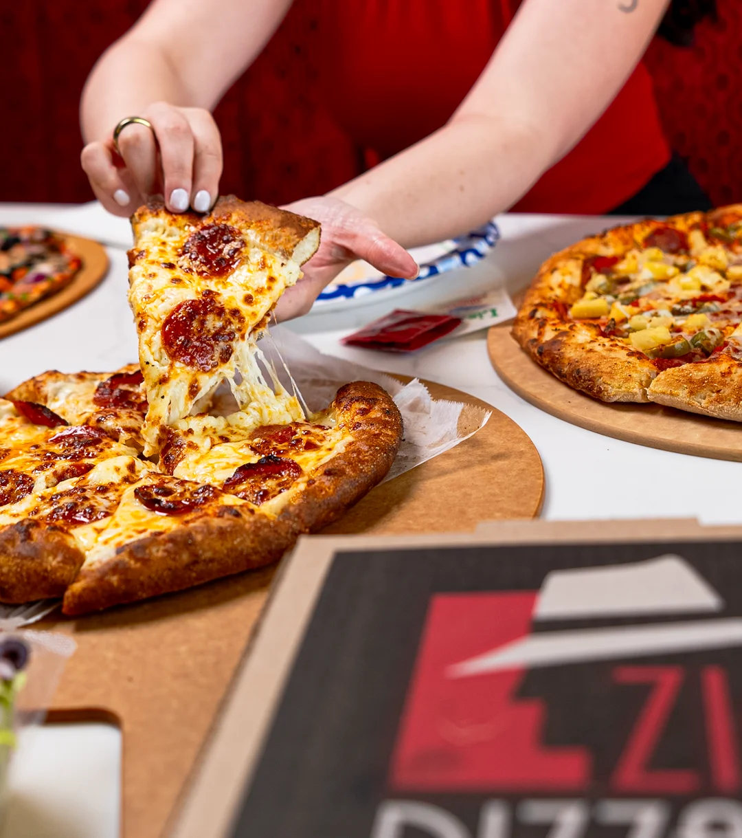A hand reaching for a slice of pepperoni pizza with melted cheese.