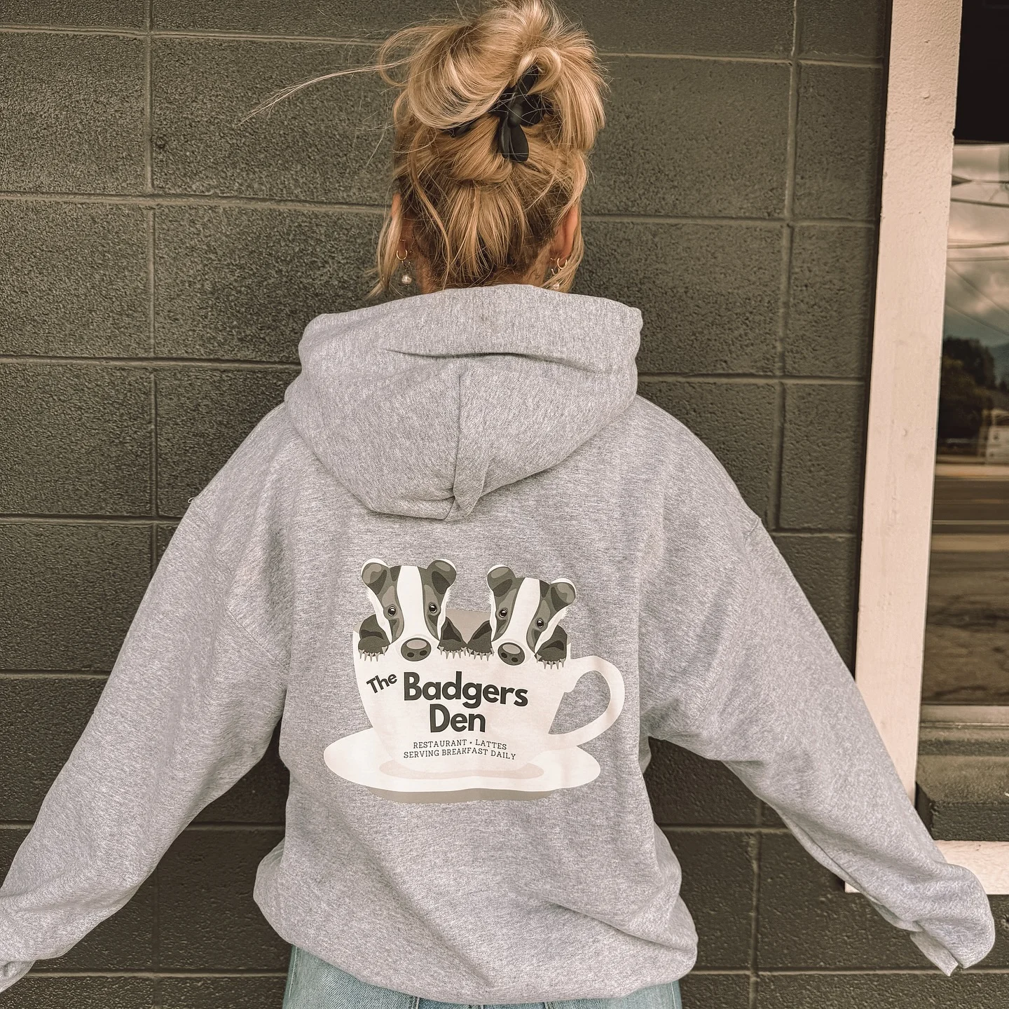 Person wearing a hoodie with Badgers Den logo and coffee cup design