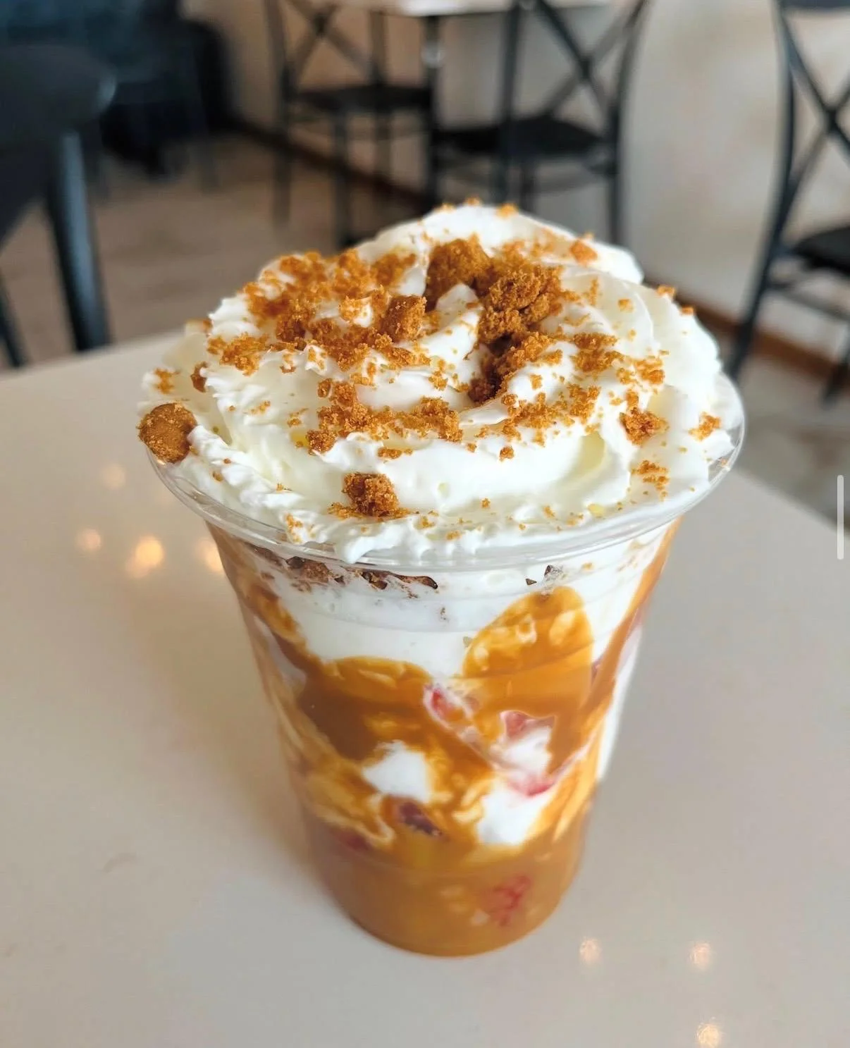 A layered dessert in a clear cup featuring chocolate, strawberries, and crunchy toppings, held against a backdrop of illuminated signage.