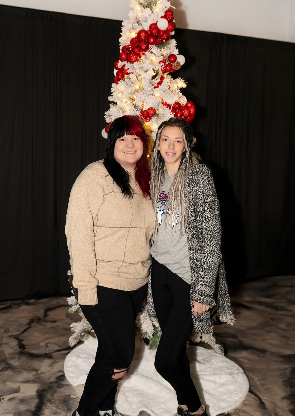 Two friends posing by a festive Christmas tree