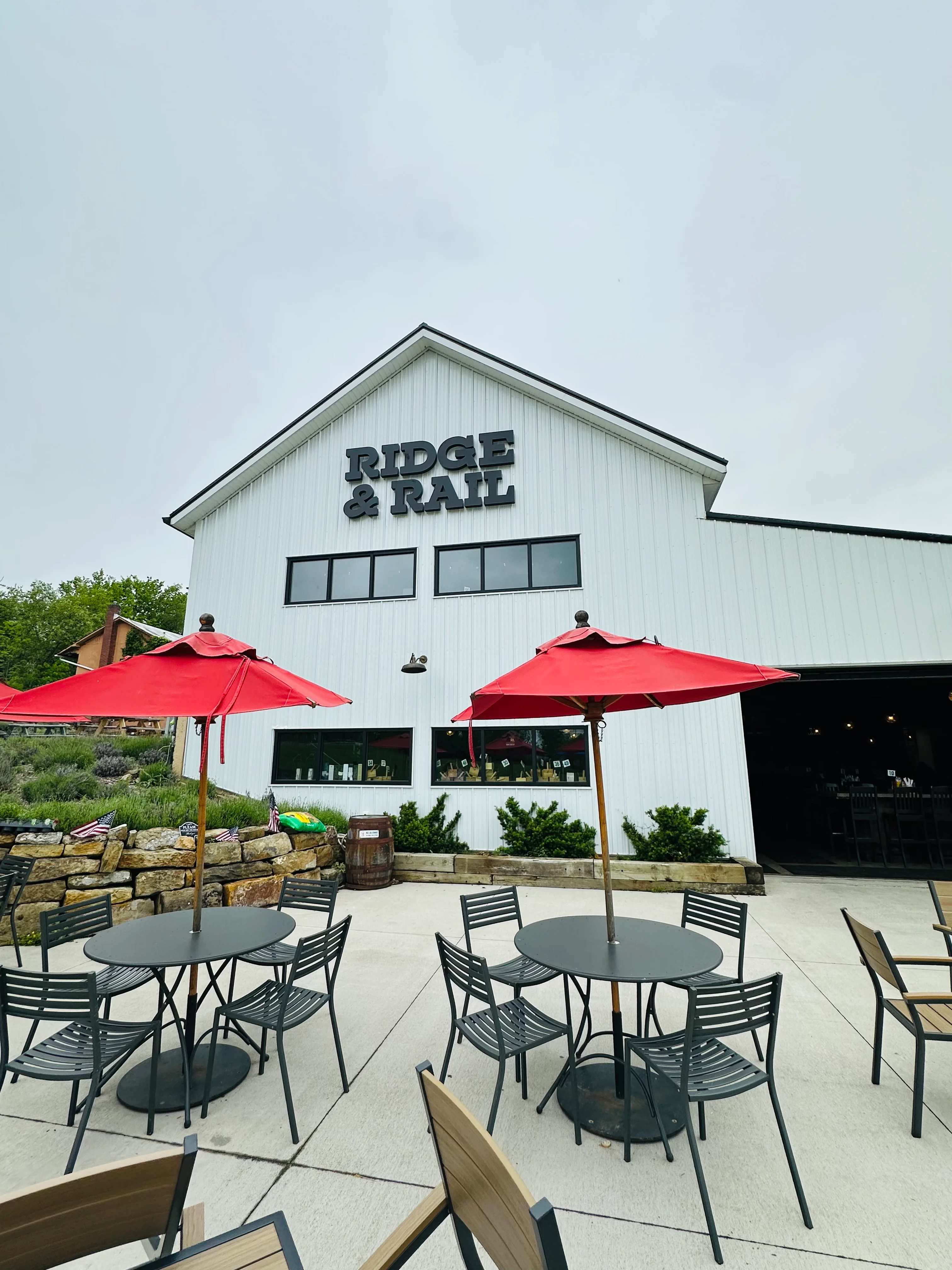 The exterior of a building with the name 'Ridge & Rail' prominently displayed, featuring outdoor seating under red umbrellas.