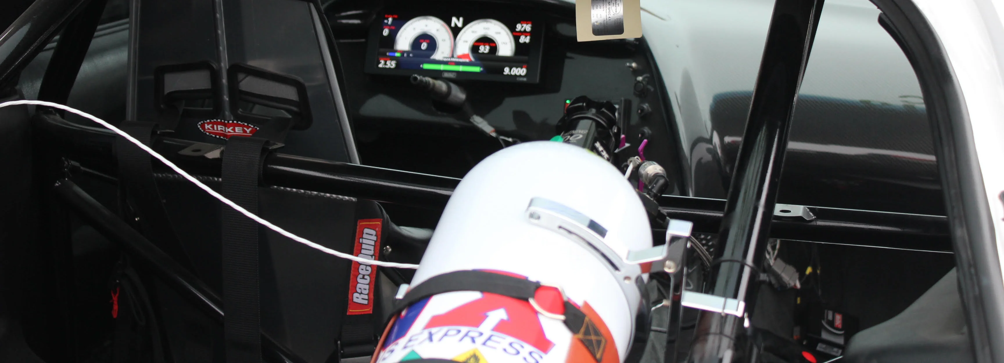 Interior view of a race car cockpit with digital dashboard and safety equipment