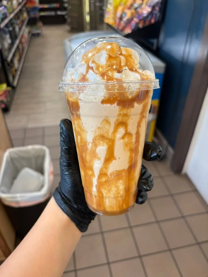 A creamy dessert drink in a clear cup, topped with whipped cream and drizzled with caramel sauce.