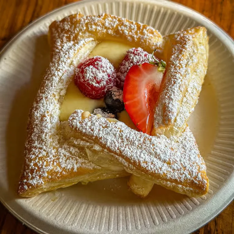 A delicious pastry topped with powdered sugar, fresh strawberries, raspberries, and blueberries, served on a plate.