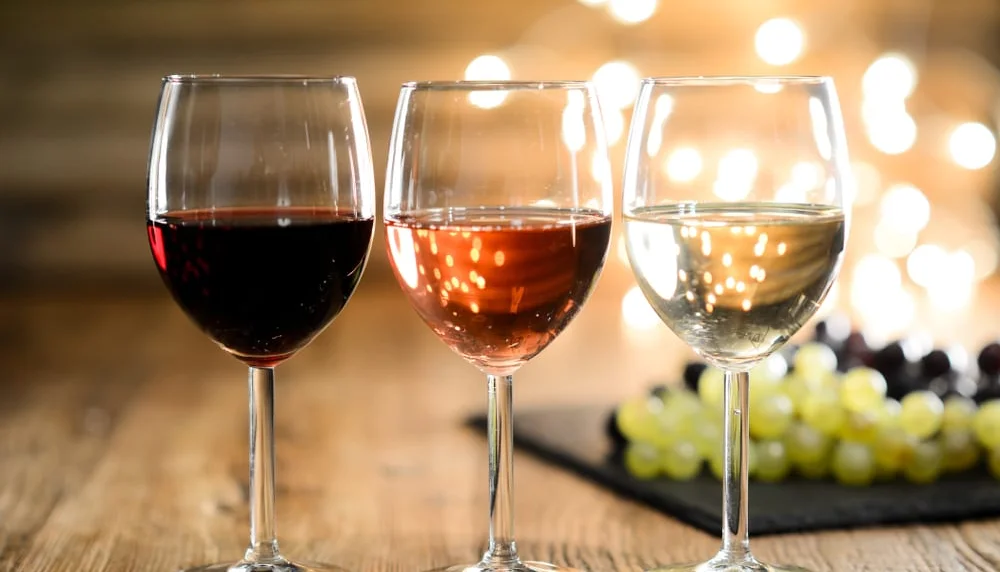 Three wine glasses with red, rosé, and white wine on a wooden table