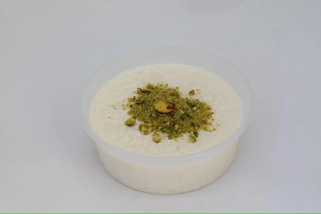 A white bowl containing a creamy dessert topped with crushed pistachios and a whole nut.