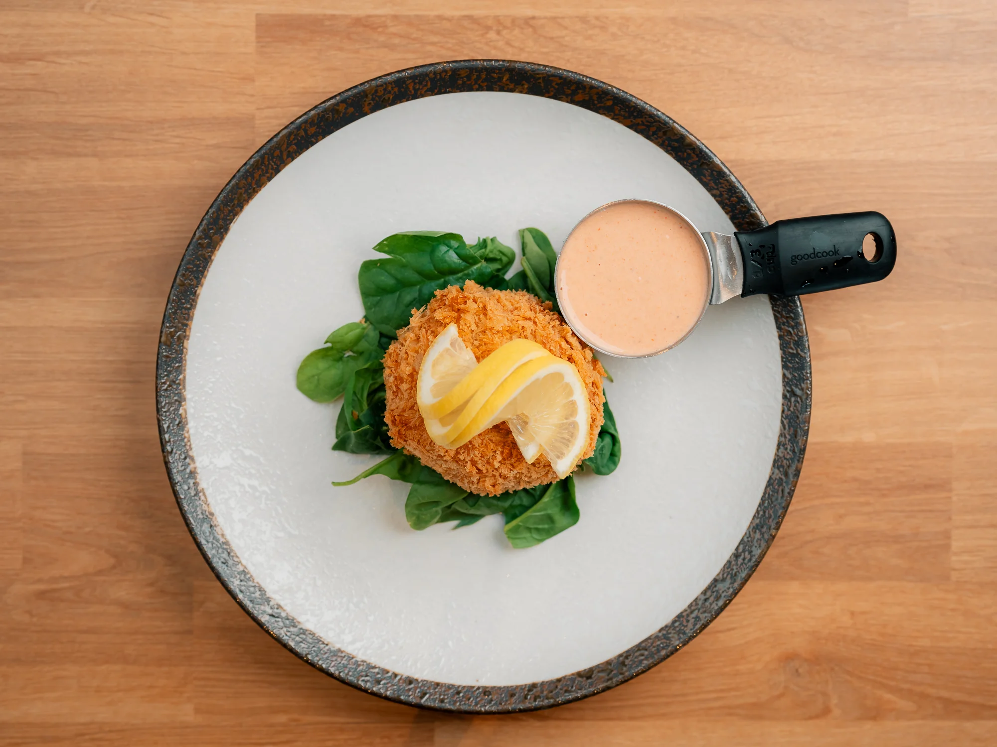 Crispy crab cake with lemon and sauce on a bed of spinach