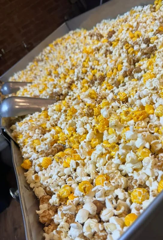 A close-up of vibrant orange popcorn, with a scoop resting on top, showcasing a variety of popcorn flavors.