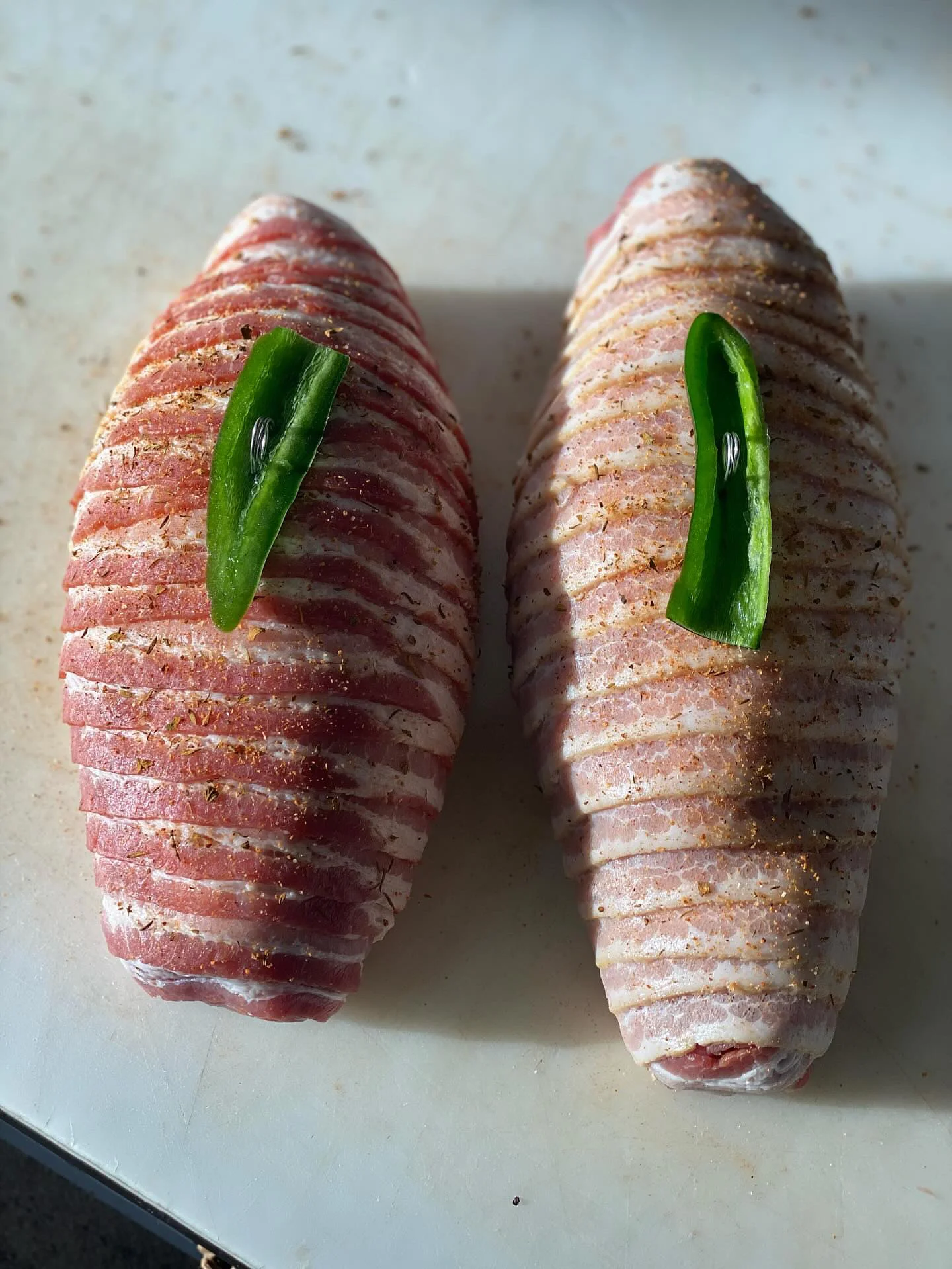 Two bacon-wrapped meatloafs with green pepper garnish on a cutting board.