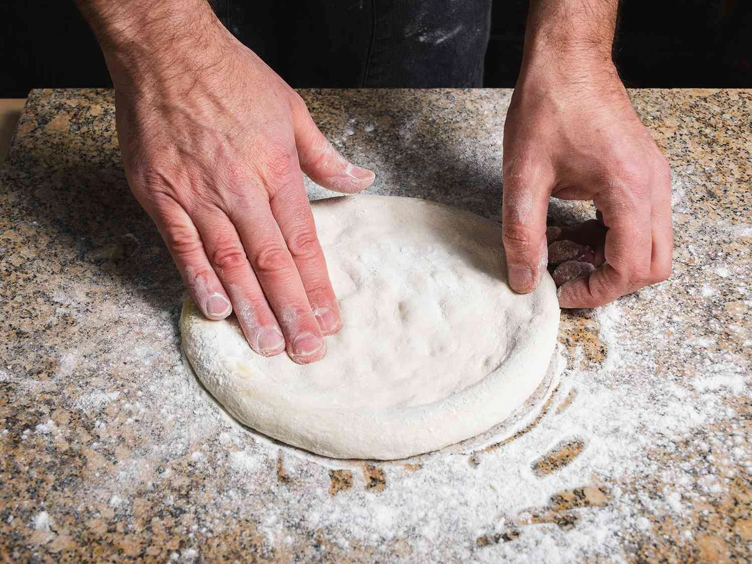 Chef shaping pizza dough on a floured countertop