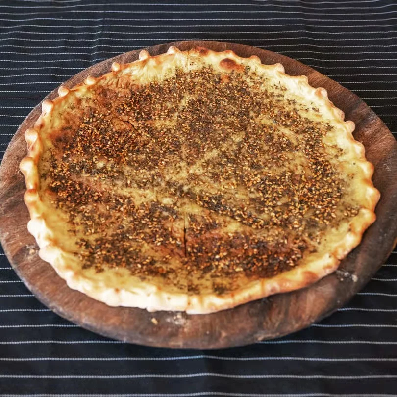 A round flatbread topped with herbs and spices on a wooden platter.
