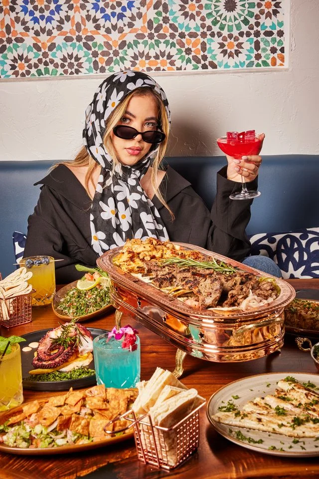 Guest enjoying a red cocktail beside a Mediterranean feast at Sufrat Grill.