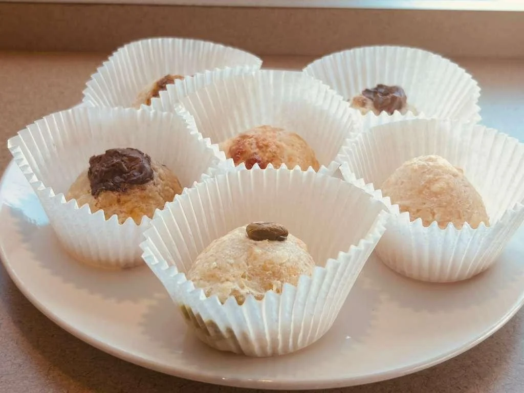 A plate of assorted sweet treats, each in a white paper cup. The sweets are round and vary in color and toppings.