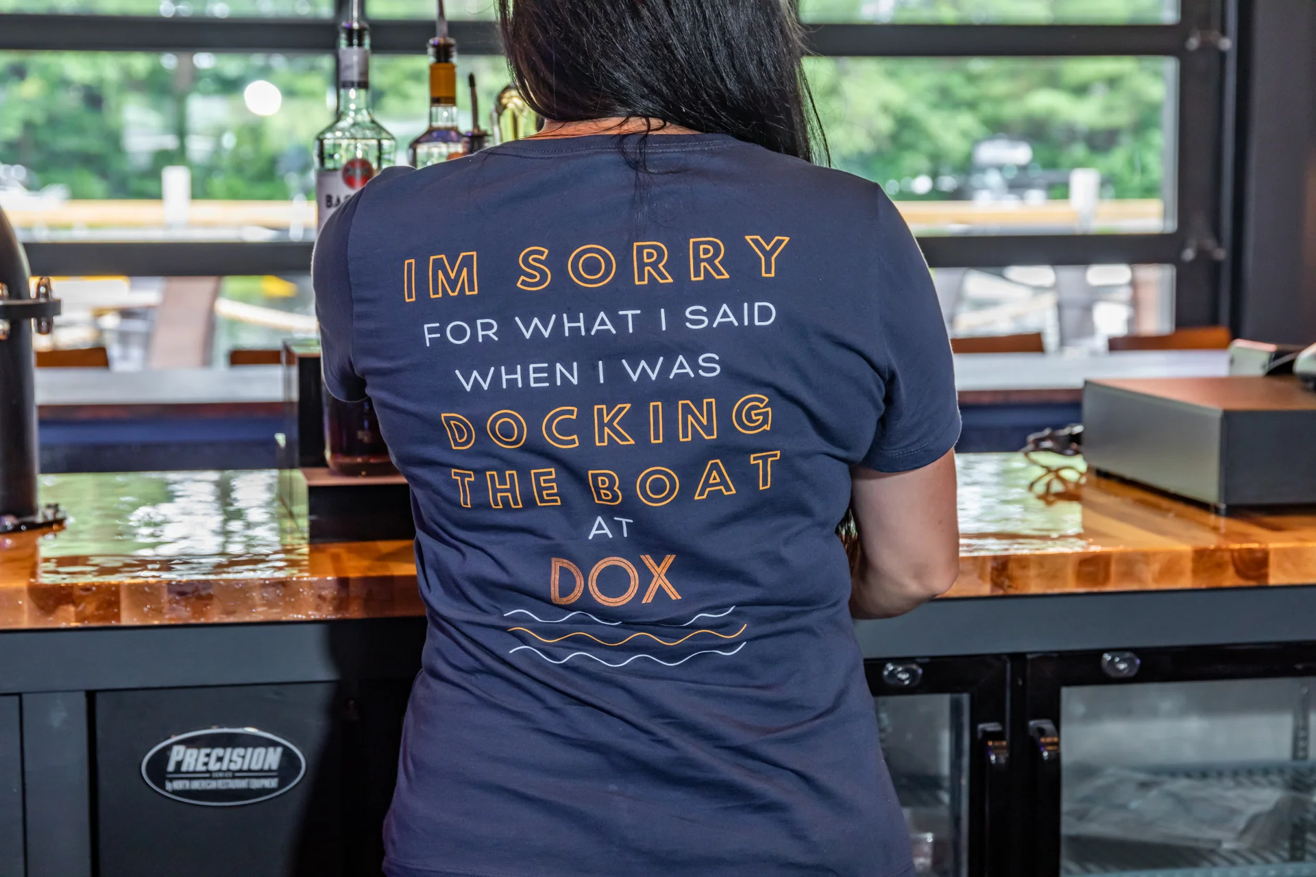 Bartender wearing humorous shirt at a lively bar