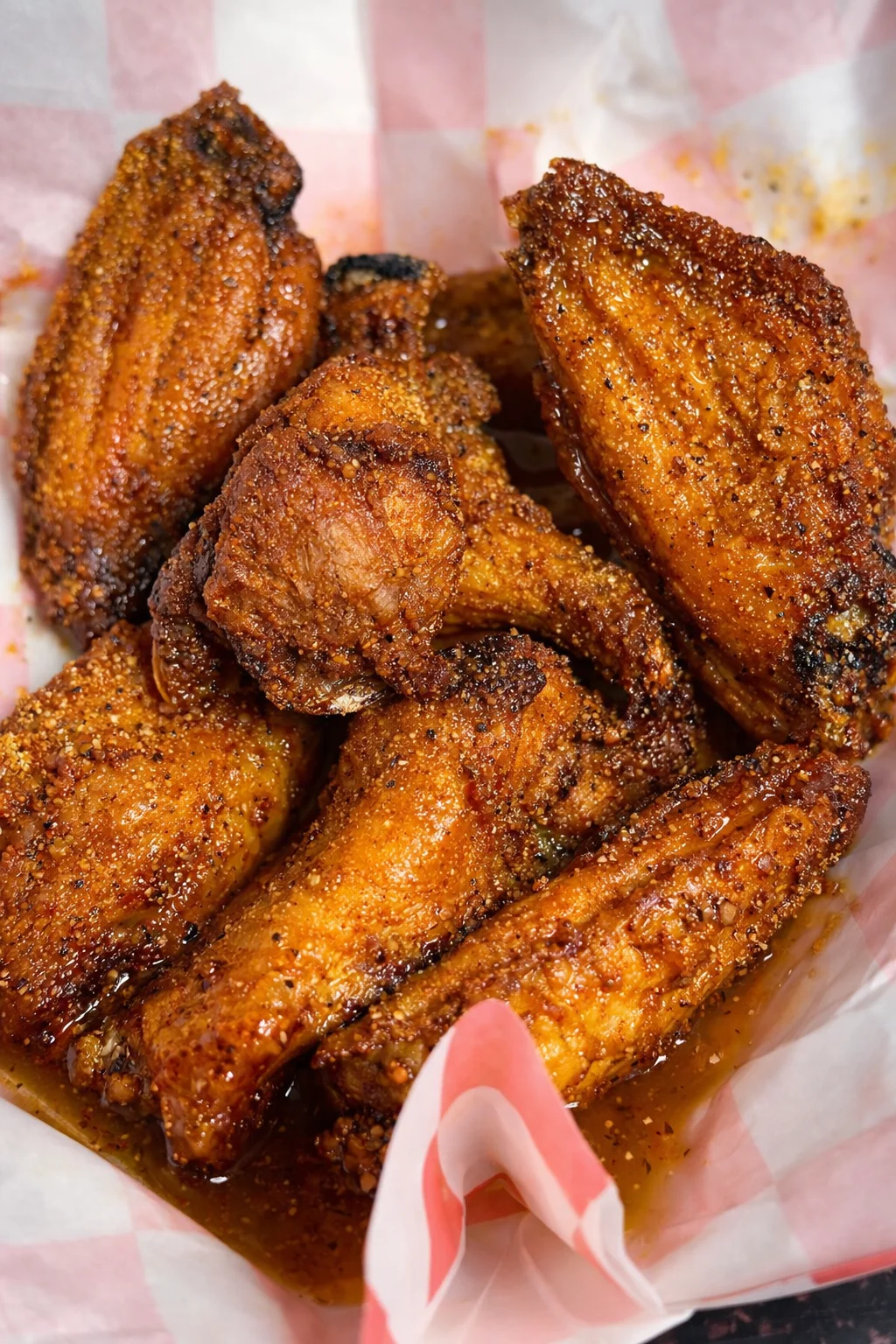 An assortment of fried foods including wings, tenders, fries, and a sandwich served in baskets with pink checkered paper.