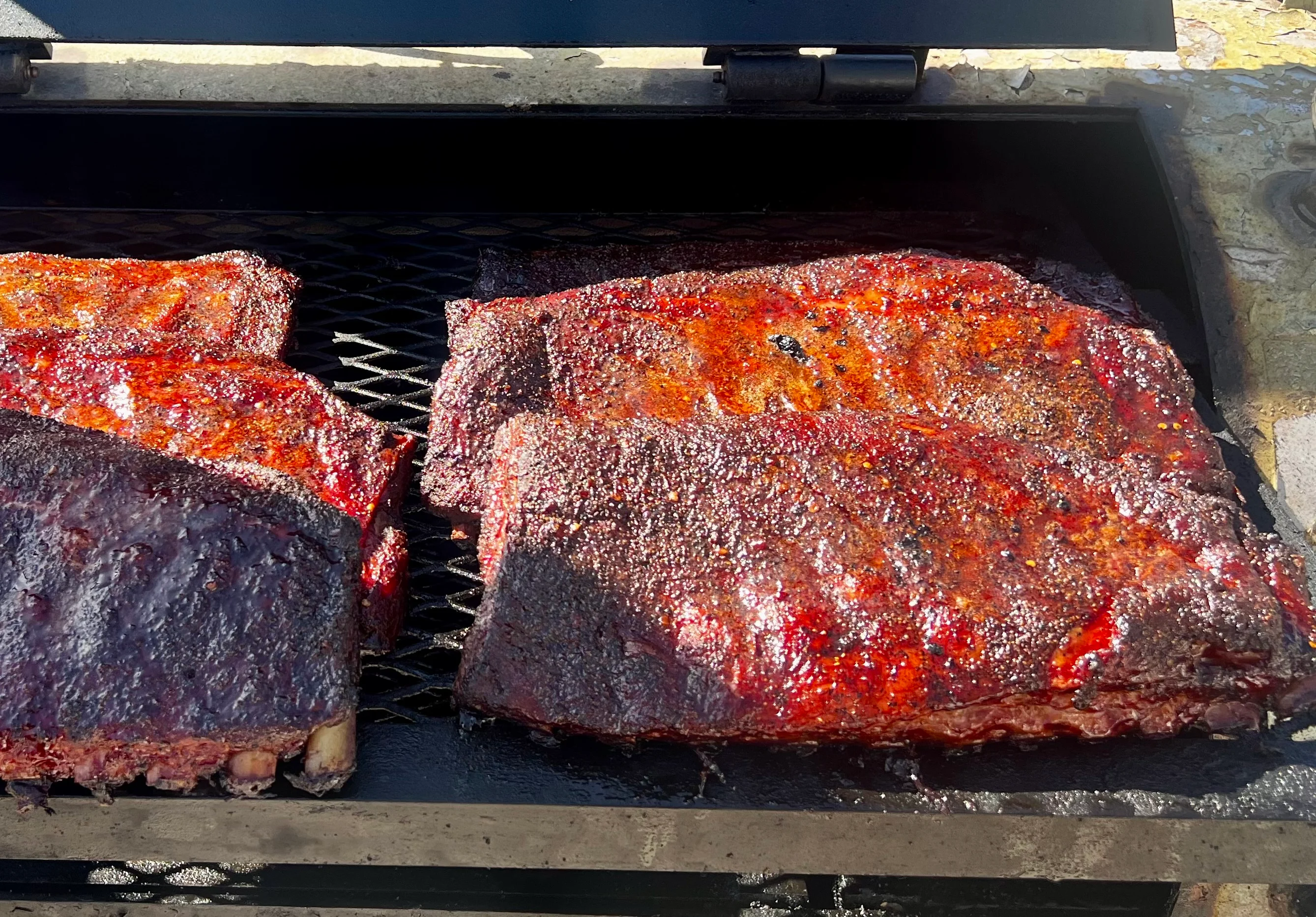 A selection of smoked ribs placed on a grill, showcasing a glossy, charred finish.