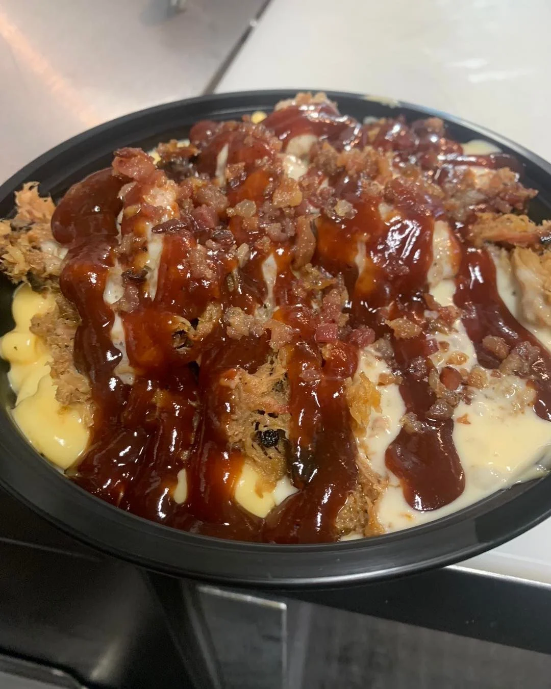 A bowl filled with creamy mashed potatoes topped with pulled pork, barbecue sauce, and crispy bacon bits.