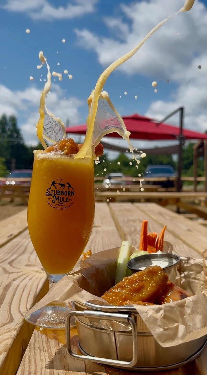 Craft cocktail with a splash and chicken wings on a wooden table