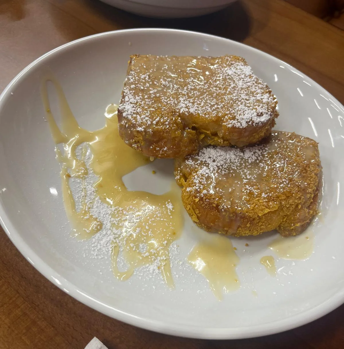 Two pieces of French toast drizzled with syrup and powdered sugar.