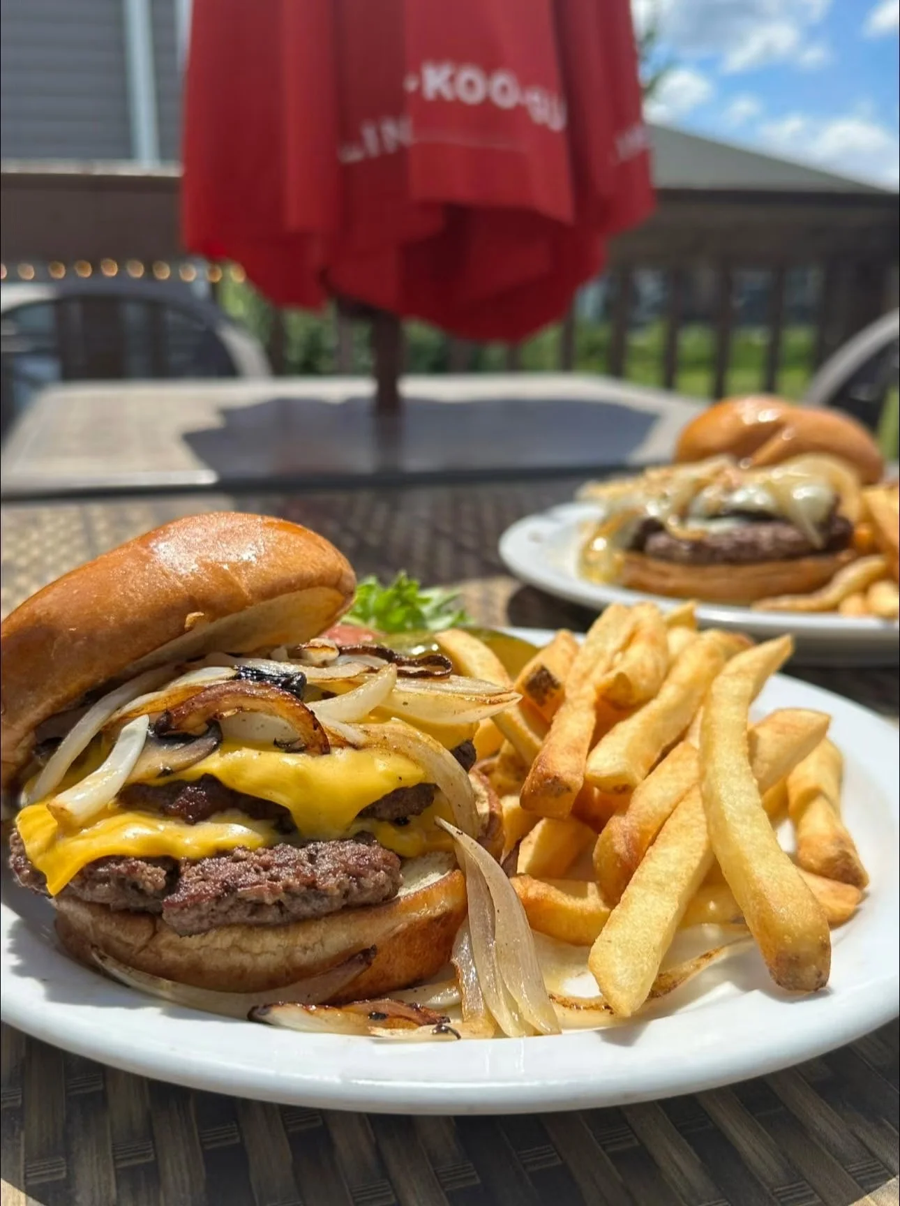 Juicy cheeseburger with grilled onions and fries on a sunny patio