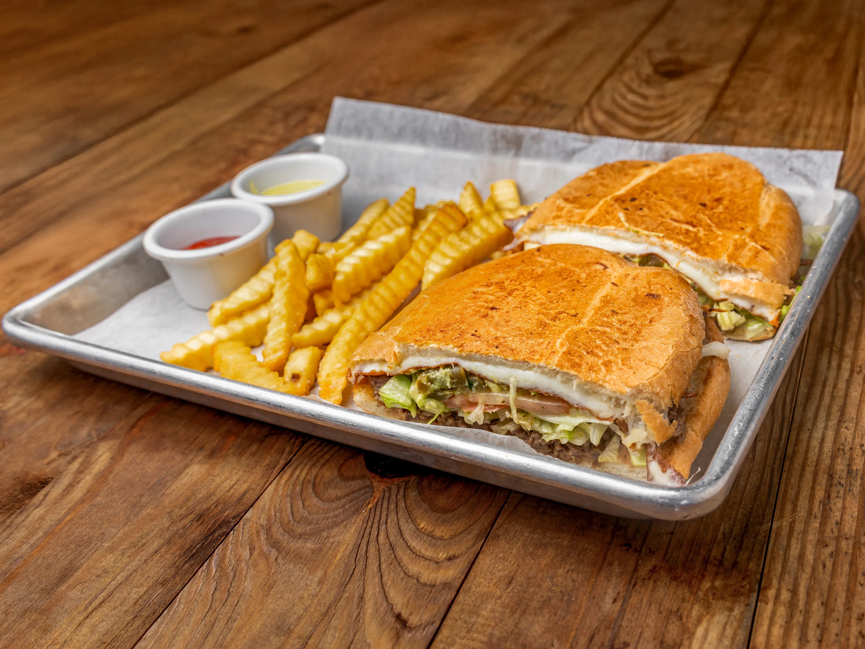 A plate featuring two sandwiches accompanied by crispy crinkle-cut fries and two dipping sauces.