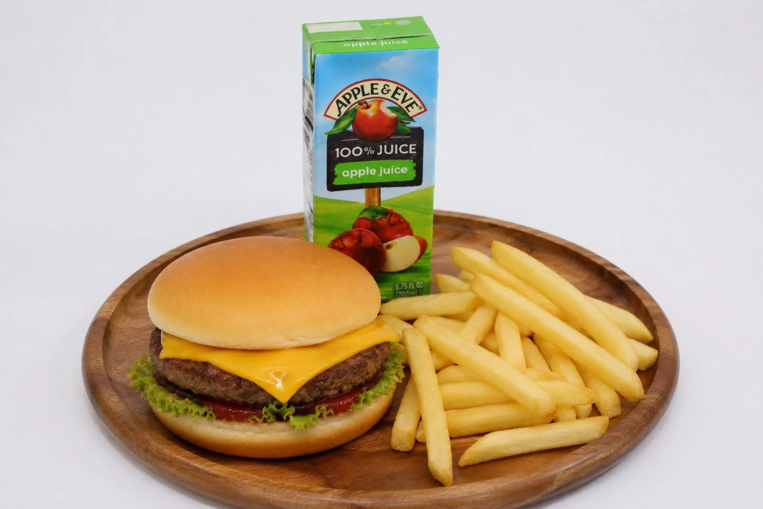 A cheeseburger with a slice of cheddar cheese, served alongside French fries and a carton of apple juice. The meal is placed on a wooden plate.