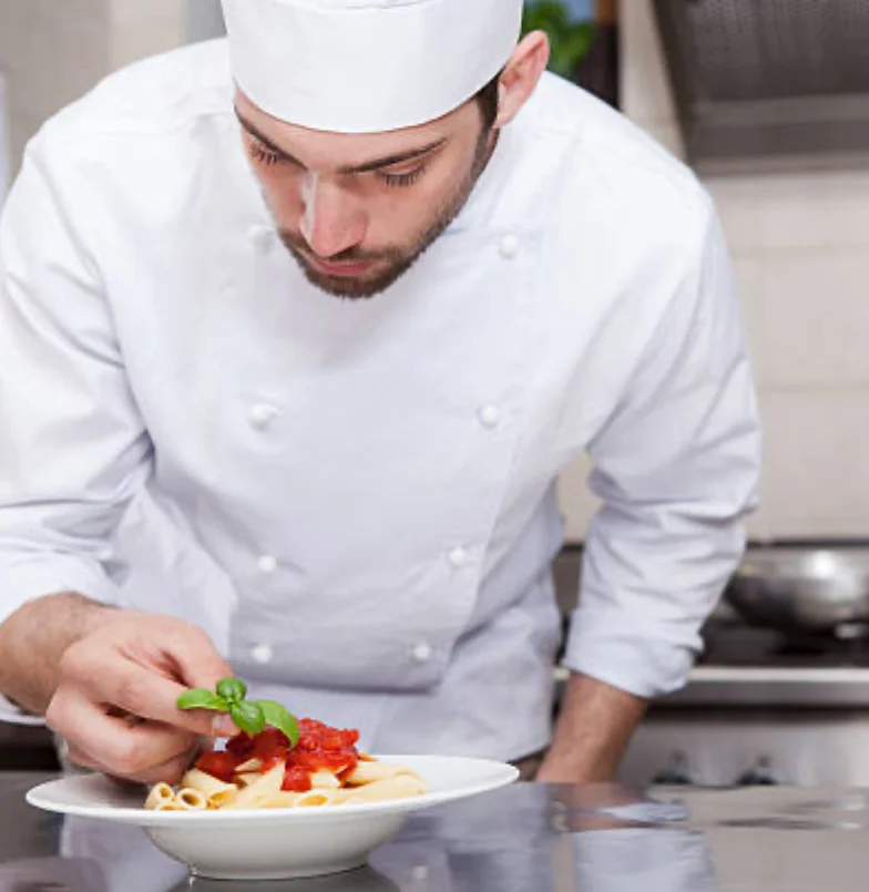 Chef plating Italian pasta with tomato sauce and basil