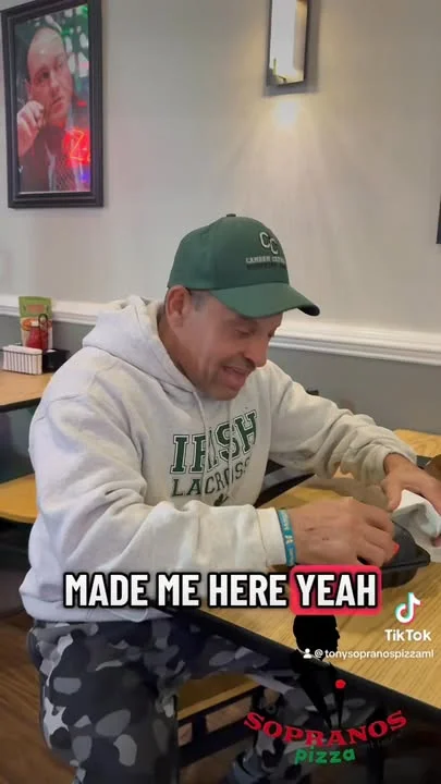 A person wearing a hoodie and cap is focused on something at a table in a casual dining setting.