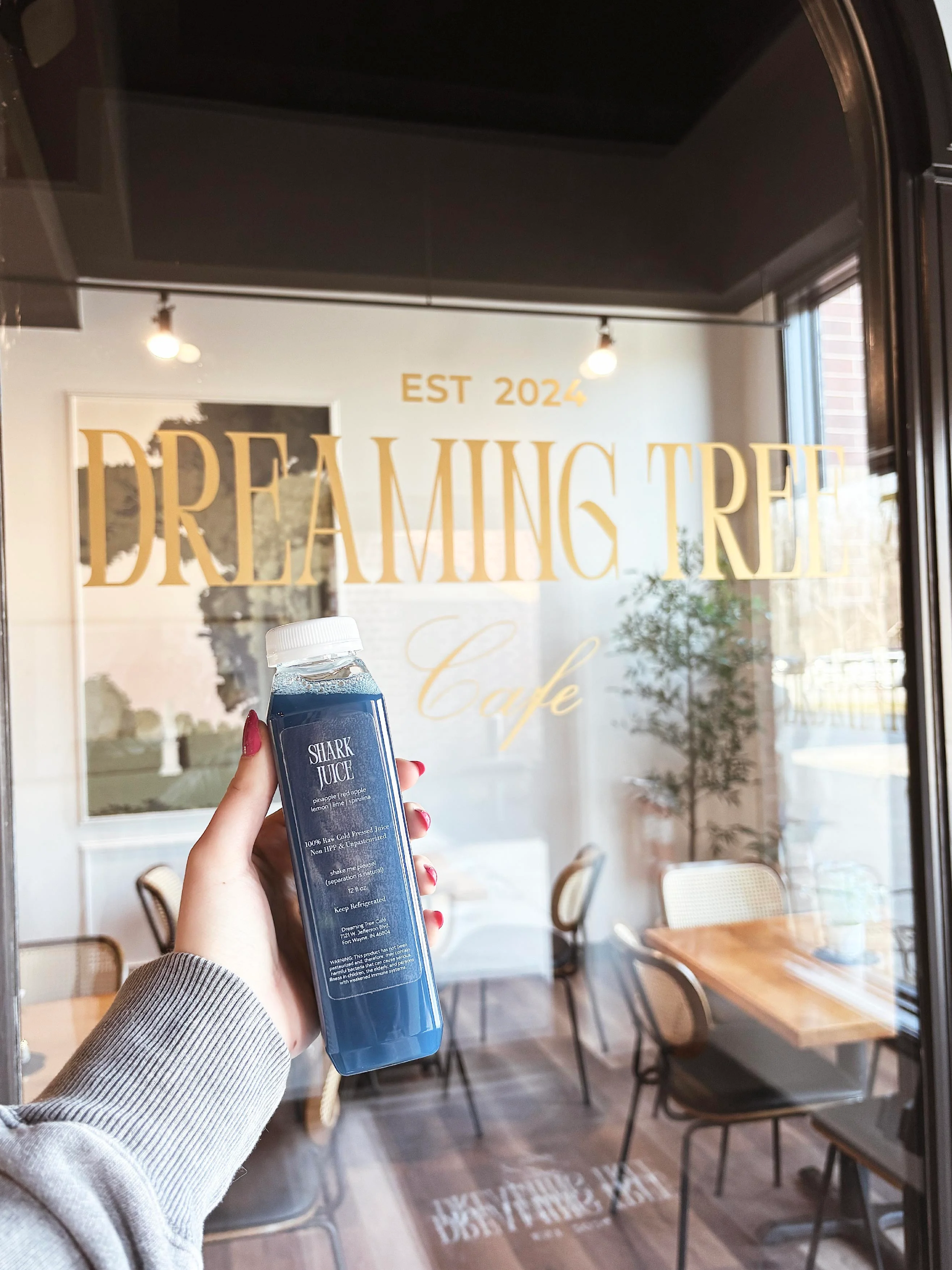 Hand holding a blue juice bottle in a cafe with modern decor